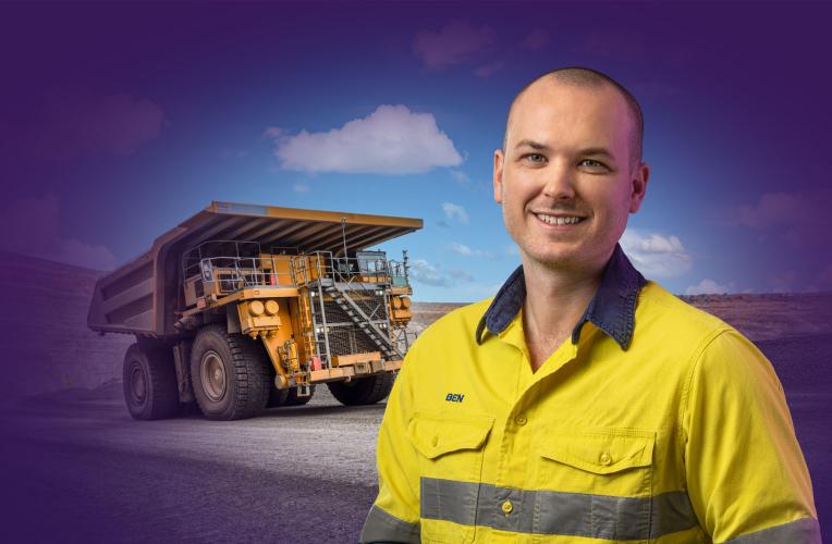Man in yellow high-vis shirt stands in front of earth-moving truck