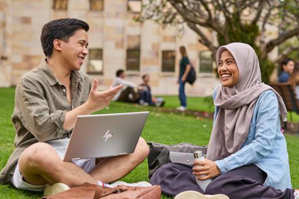 2 students sitting on Great Court lawn with laptops.